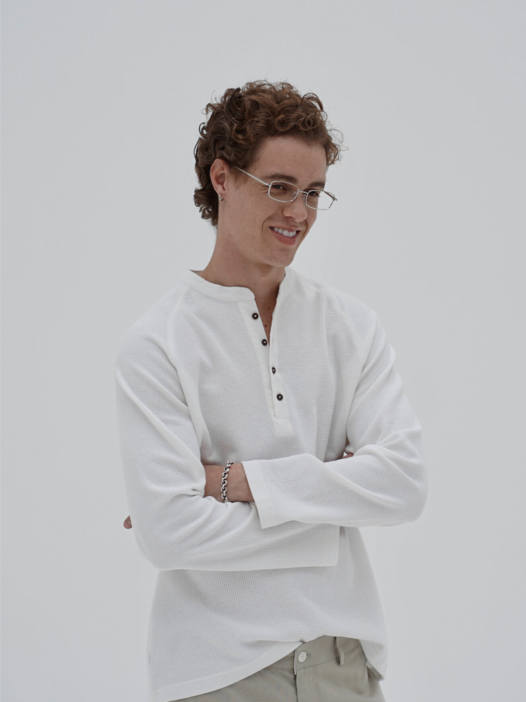 A man wearing a white long-sleeve henley shirt and light khaki pants by inknots.