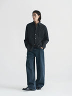 A model stands against a plain light gray studio background wearing a dark charcoal button-up shirt with a subtle grid pattern, paired with dark blue wide-leg jeans from Inknots.