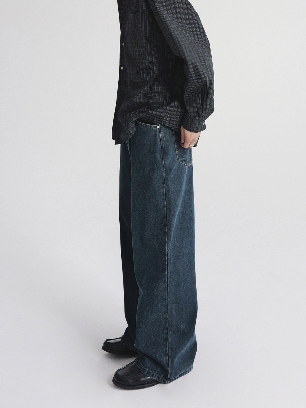 A person shown from the chest down wearing dark blue wide-leg denim jeans, a dark patterned button-up shirt from Inknots, standing against a light gray studio background.