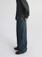 A person shown from the chest down wearing dark blue wide-leg denim jeans, a dark patterned button-up shirt from Inknots, standing against a light gray studio background.