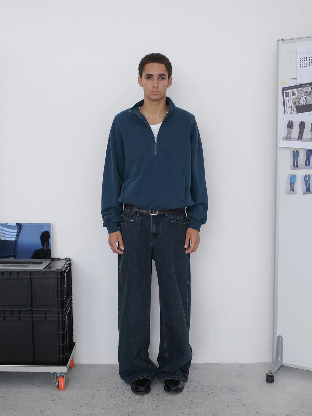A man stands facing forward wearing a dark navy quarter-zip pullover, dark wide-leg jeans from Inknots.