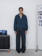 A man stands facing forward wearing a dark navy quarter-zip pullover, dark wide-leg jeans from Inknots.