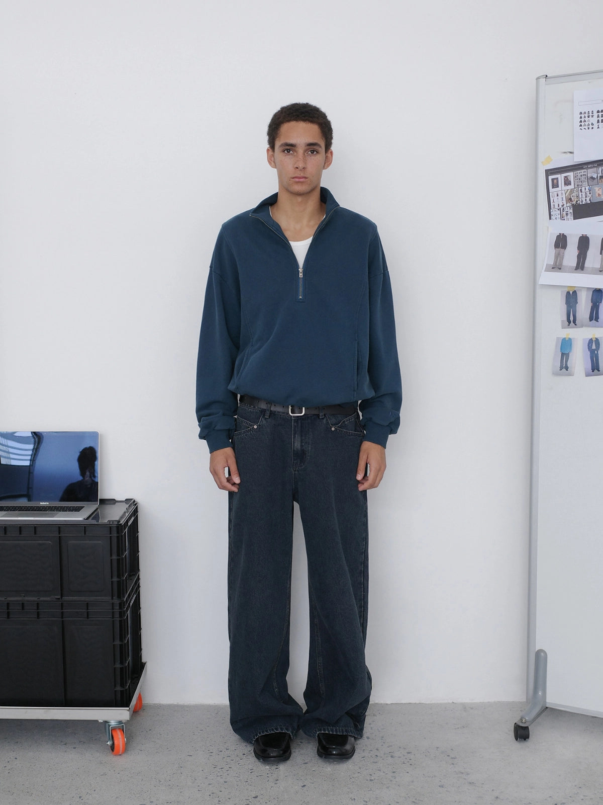 A man stands facing forward wearing a dark navy quarter-zip pullover, dark wide-leg jeans from Inknots.