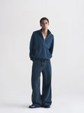 A man modeling a dark blue quarter-zip pullover and matching wide-leg jeans against a plain light gray studio background.