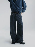A person wearing dark wide-leg denim jeans with a brown belt, paired with a navy quarter-zip pullover from Inknots, photographed against a light gray studio background.